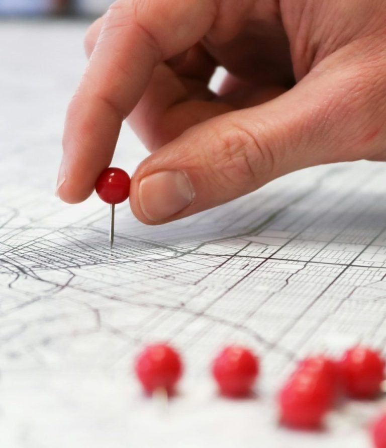 Eine Hand sticht eine Pinnadel in einen Stadtplan.