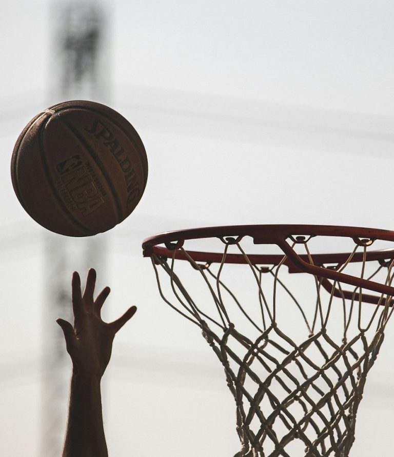 Ein Hand wirft einen Basketball, der in Richtung des Korbs fliegt.