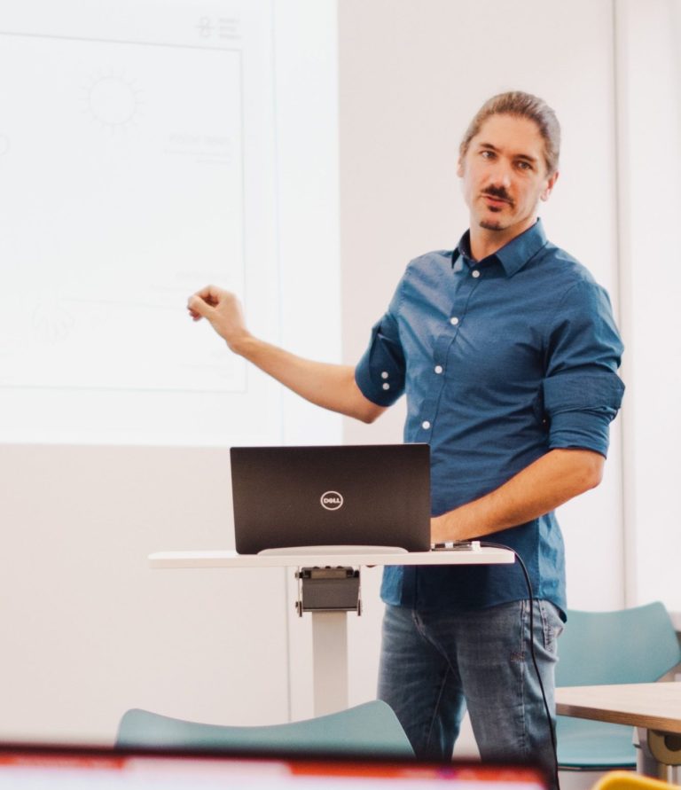 Mann präsentiert an einem Laptop, zeigt auf eine Grafik an der Wand.