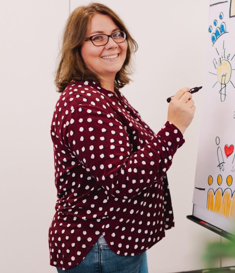 Frau mit Brille und gepunktetem Hemd, die an einem Flipchart zeichnet.